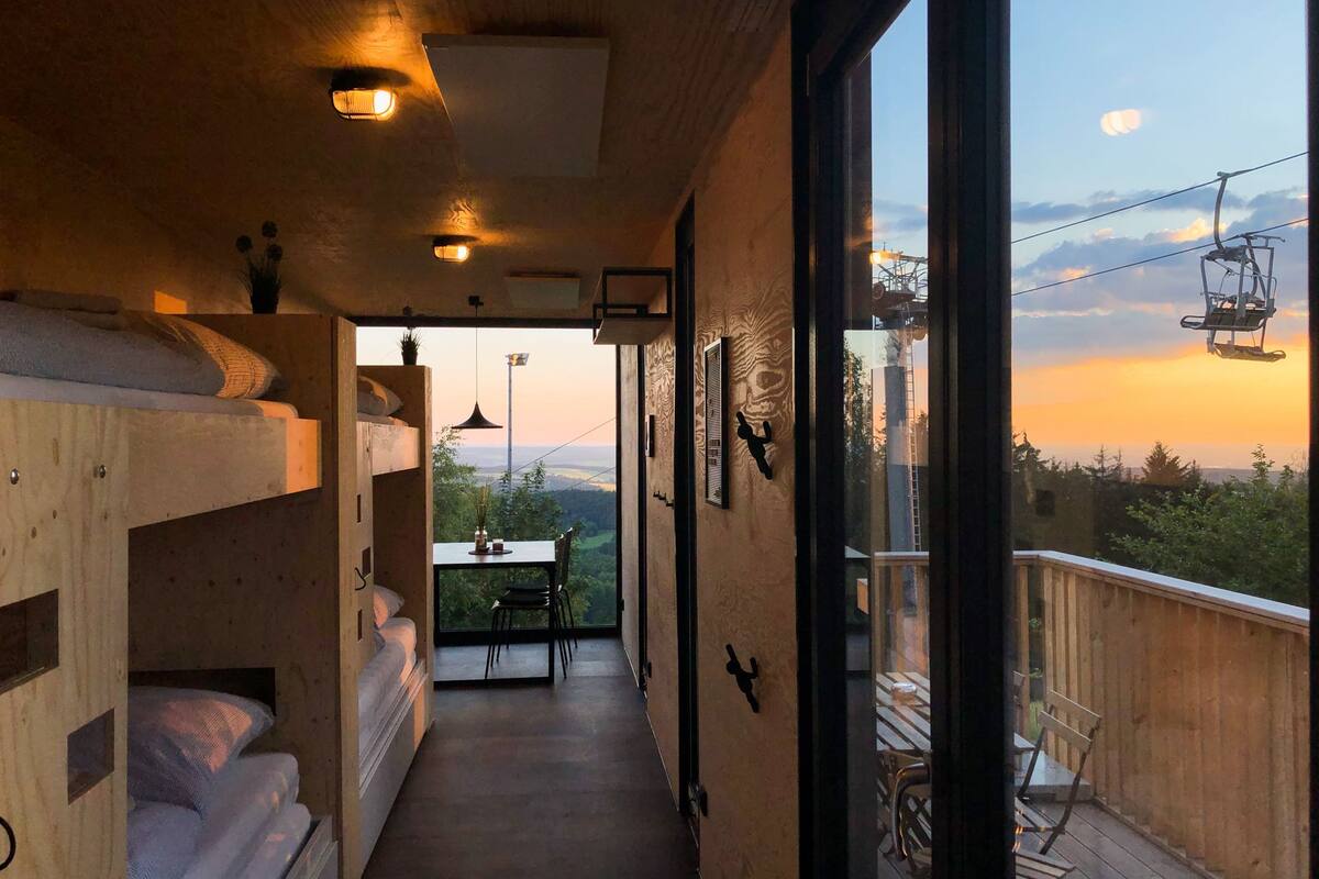 A narrow corridor with bunk beds on one side and a balcony with outdoor seating.