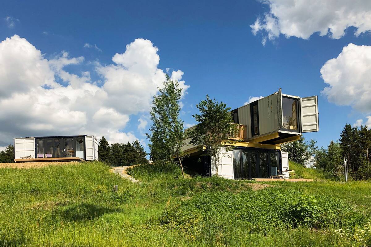 Two shipping containers repurposed as cabins with a grassy landscape and trees in the background.