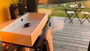 A bathroom with a white sink and a view of a grassy field with sheep. - Bergheim Container Lodges (Schoeneck)