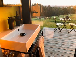 Un baño con un lavamanos blanco y vistas a un campo verde con ovejas.