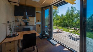 A modern kitchen with wooden cabinetry, a built-in stove, and a large window overlooking a deck. - Bergheim Container Lodges (Schoeneck)