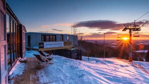 A modern building with large windows and a wooden deck, overlooking a snowy landscape with a ski lift in the background. - Bergheim Container Lodges (Schoeneck)