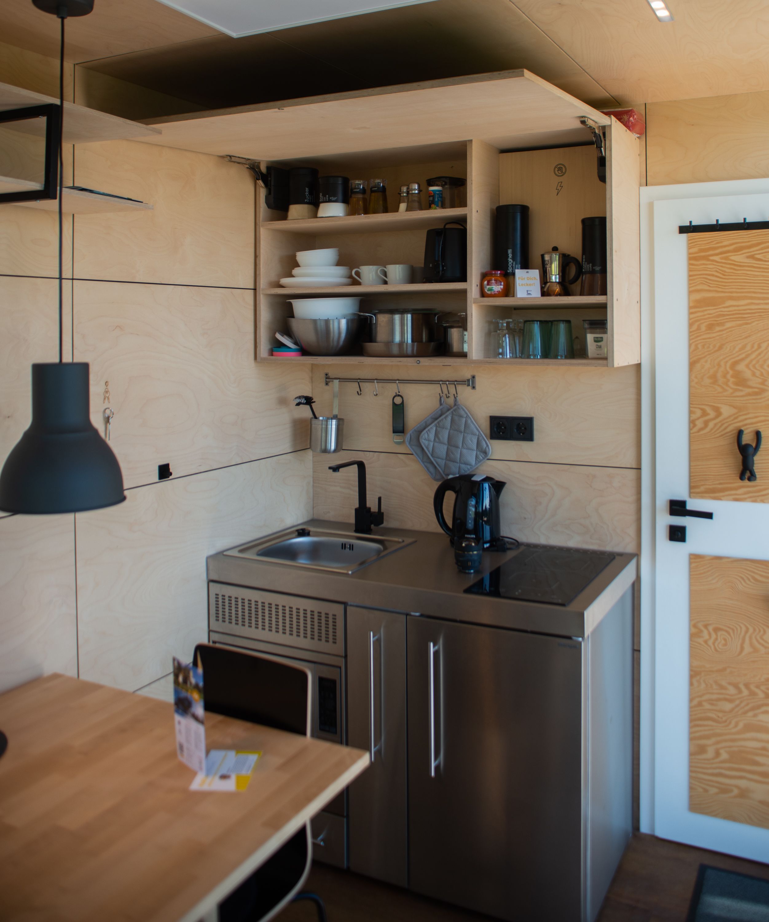 Una cucina compatta con lavandino, piano cottura ed scaffali sopra per riporre oggetti.