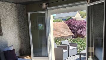 Een slaapkamer met een groot bed, een schuifdeur naar een buitenpatio met rieten meubels en uitzicht op een huis en bomen.