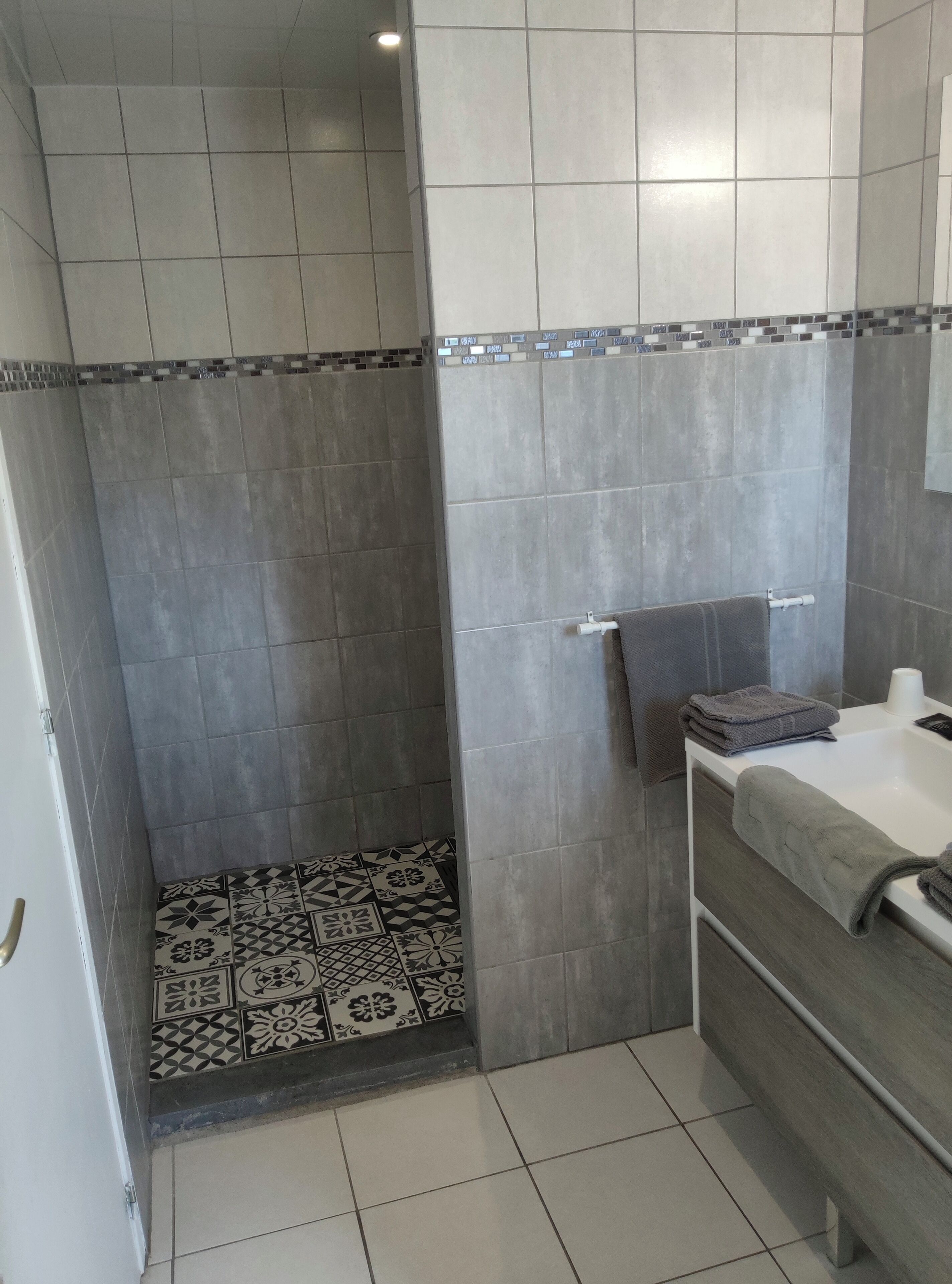 Un baño con baldosas grises, piso estampado y un lavabo blanco con toalla.