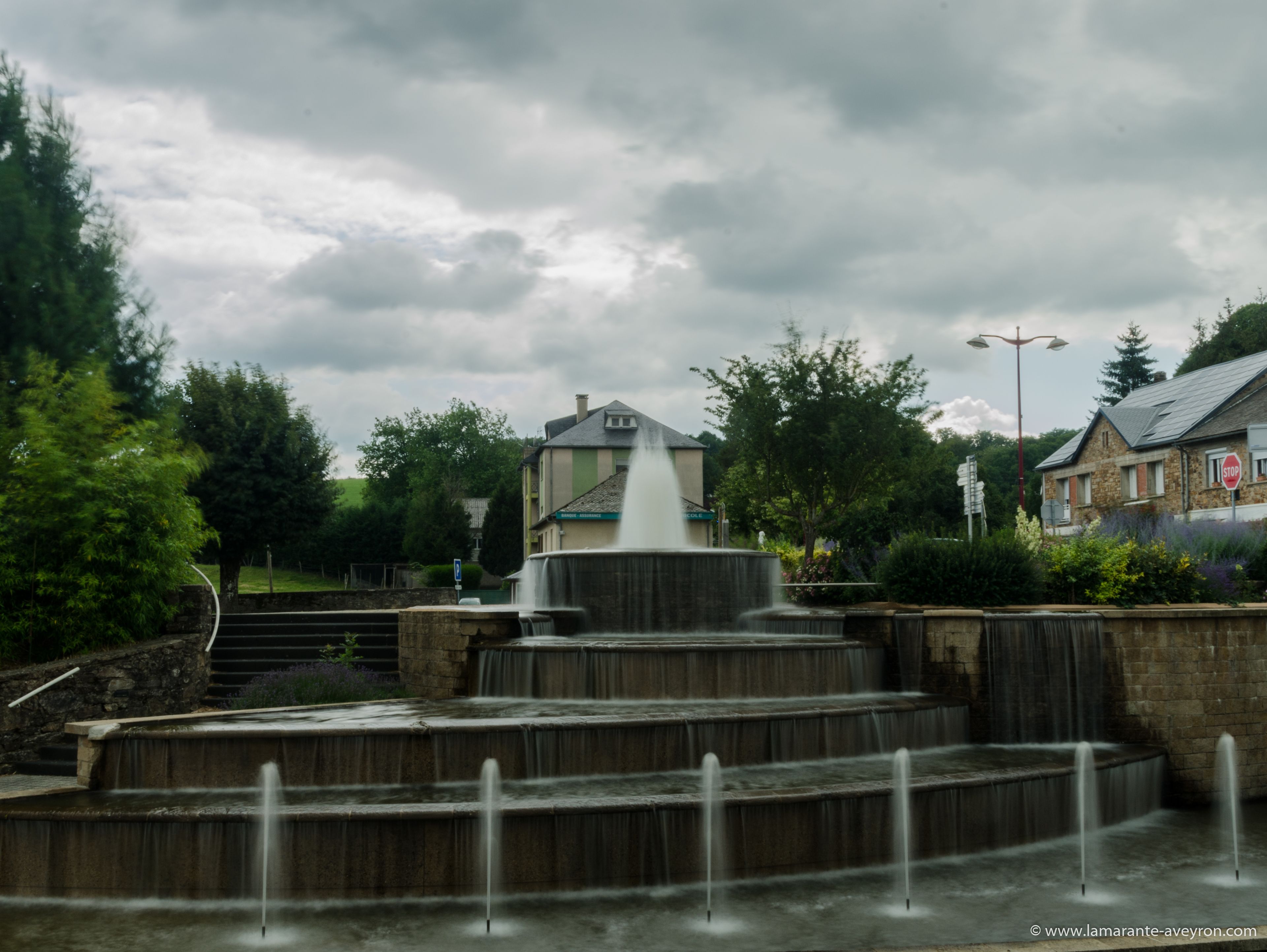 A multi-tiered fountain with water cascading down, surrounded by stone steps and greenery.