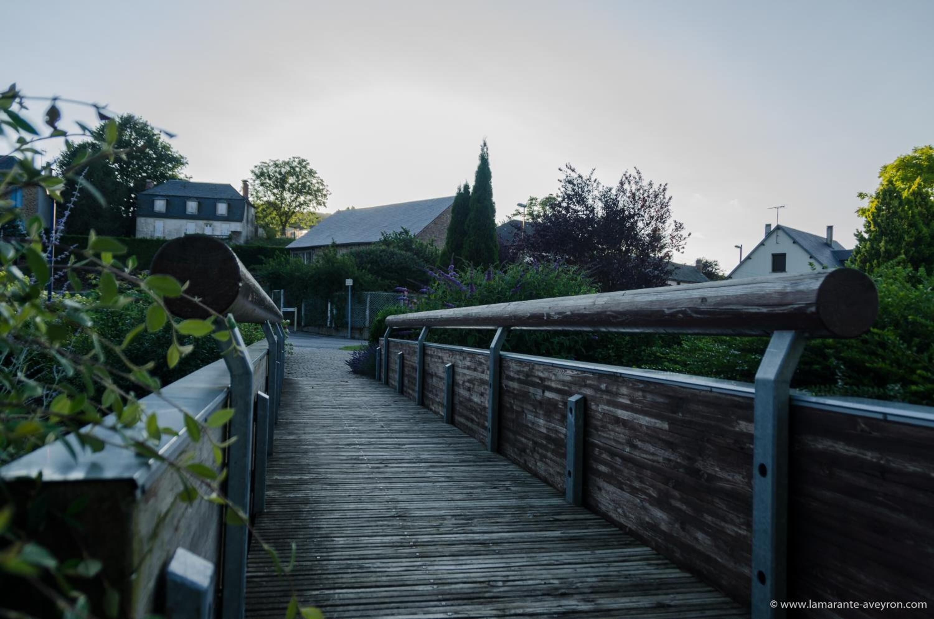 Une promenade en bois mène à un bâtiment doté d’un toit en pente, qui est entouré de verdure et d’arbres.