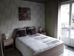 A bedroom with a bed, a nightstand, a wall-mounted artwork, and a view through a door. - L' Amarante chambres d'hôtes (Villefranche-de-Panat)