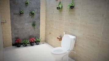 A bathroom with a white toilet, potted plants, and a tiled wall.