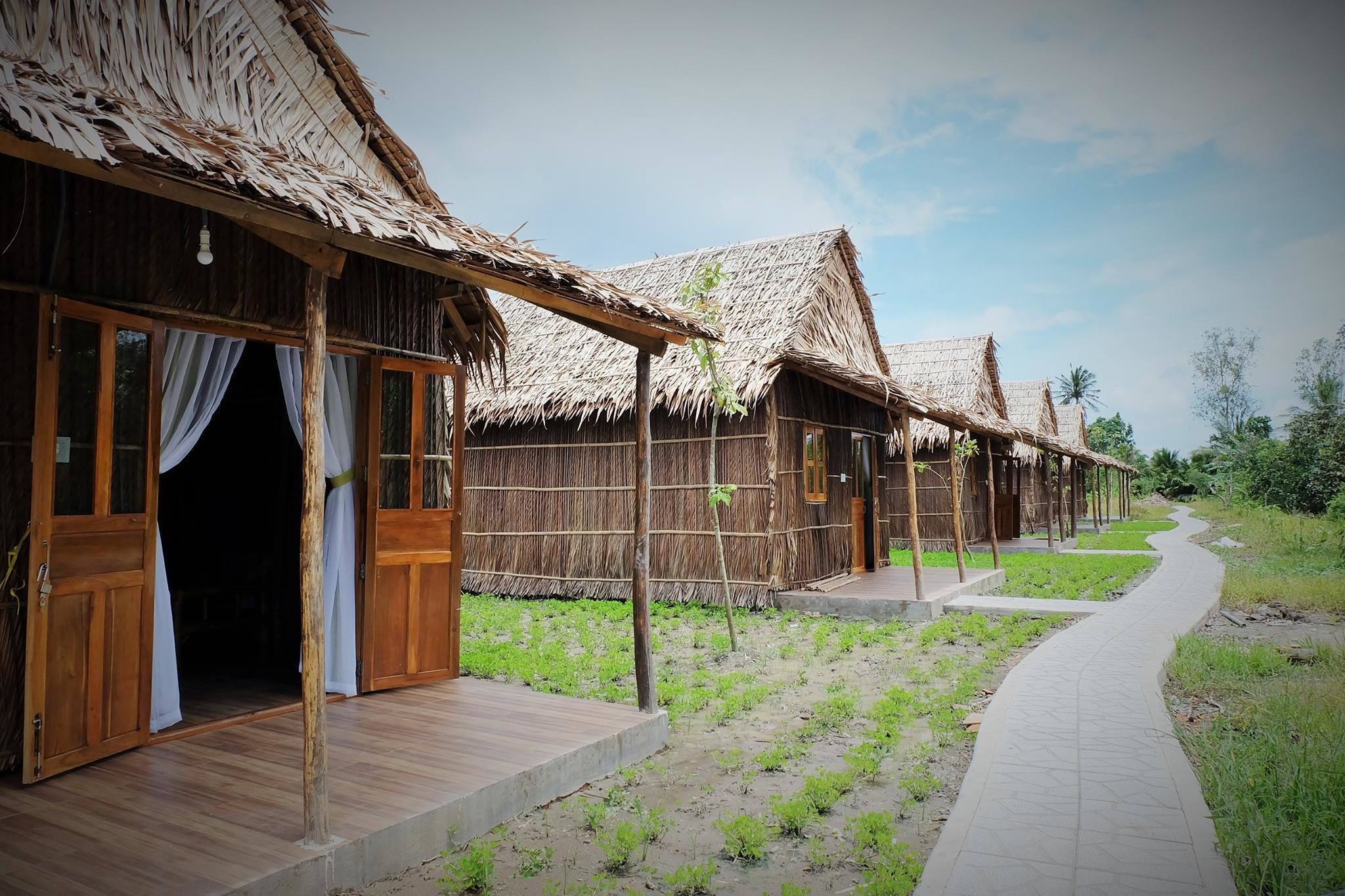 Una hilera de casas de campo con techos de paja, puertas y ventanas de madera, conectadas por un camino pavimentado.