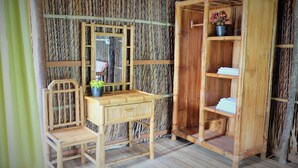 Habitación con pared de bambú, un escritorio de madera con espejo, una silla y un armario con estantes.