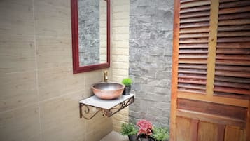 Bany amb paret de pedra, porta de fusta, rentamig blanc amb cuina de coure, mirall i plantes en testos.