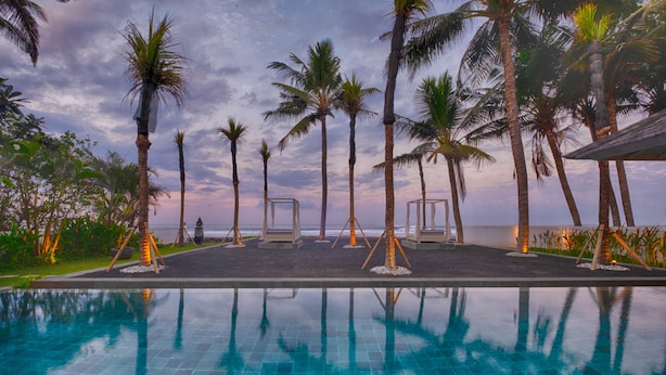 A pool area with palm trees and a view of the ocean. - Kutus Kutus Saba Beach Villa (Blahbatuh)