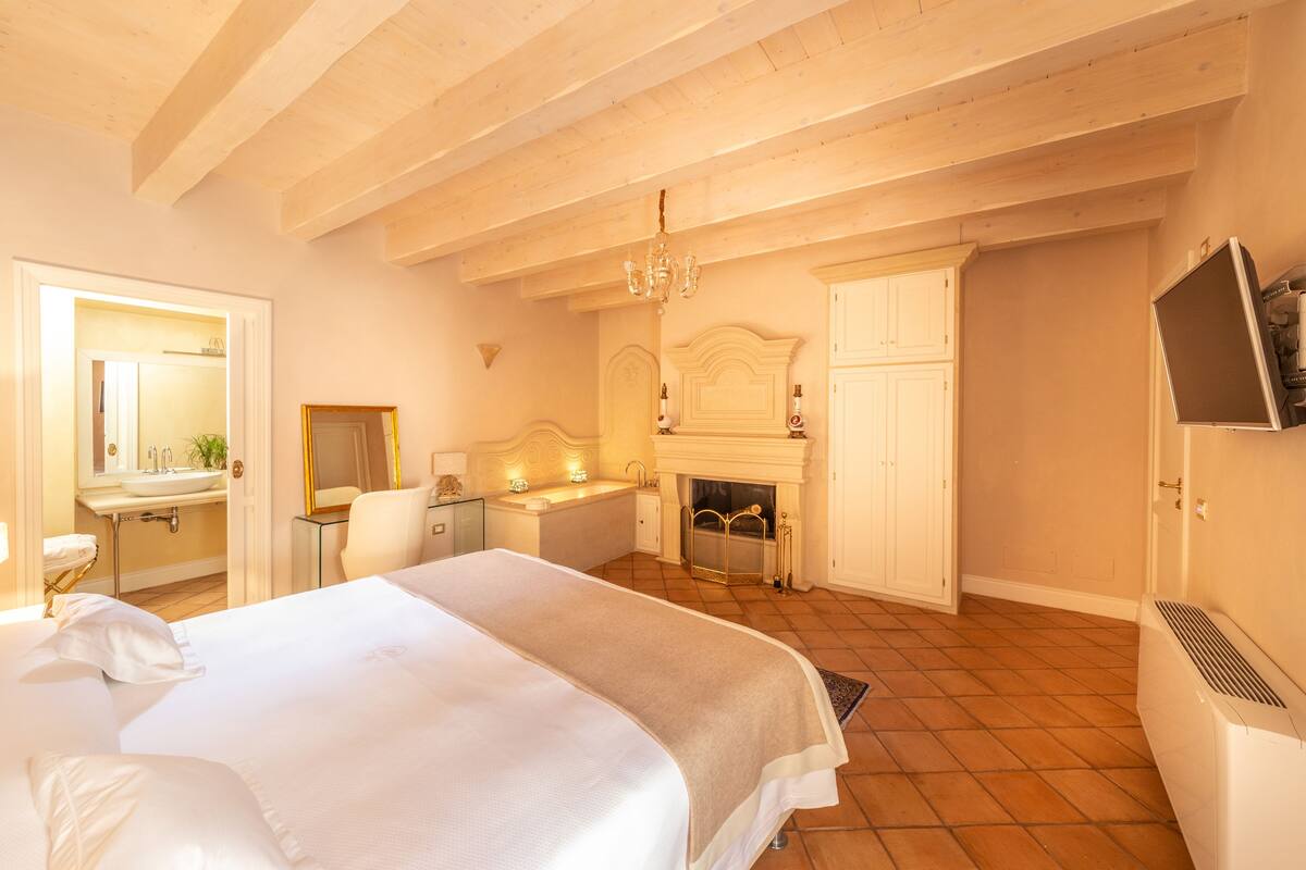 A bedroom with a large bed, a fireplace, a mirror, and a television.