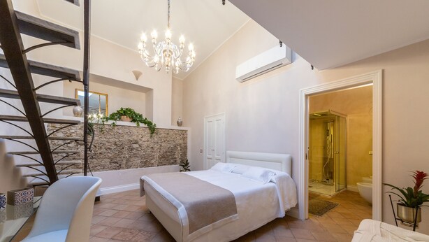 A bedroom with a bed, a chair, a staircase, a chandelier, and a bathroom with a shower. - Boutique - Lodge & Suites (Crotone)