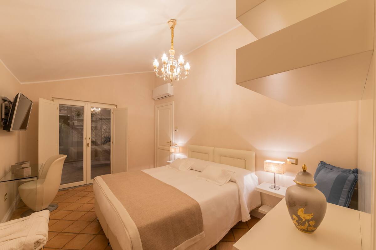 A hotel room with a large bed, a desk with a lamp, a vase, and a chair.