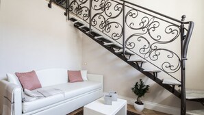 A modern living room with a white sofa, a small white side table, a patterned rug, a potted plant, and a black spiral staircase. - Boutique - Lodge & Suites (Crotone)