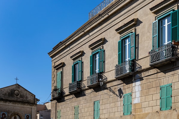 A building with multiple windows, green shutters, and balconies with wrought iron railings.