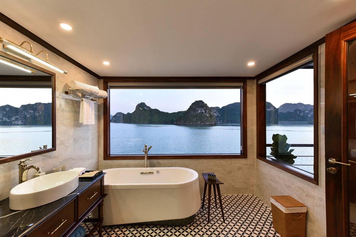Casa de banho com uma banheira grande, uma pia e uma janela com vista para um lago e montanhas.