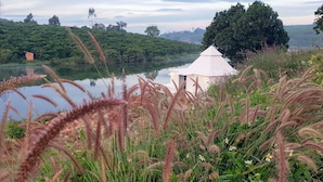 A serene lakeside view with a small white structure, possibly a gazebo, surrounded by lush greenery and tall grasses. - Ho Gia Trang (Tan Ha Lam Ha)
