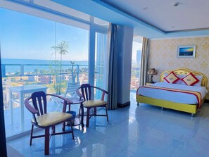 A hotel room with a bed, two chairs, a large window, and a view of the city. - Sunrise Ninh Thuan Hotel (Ninh Chu)