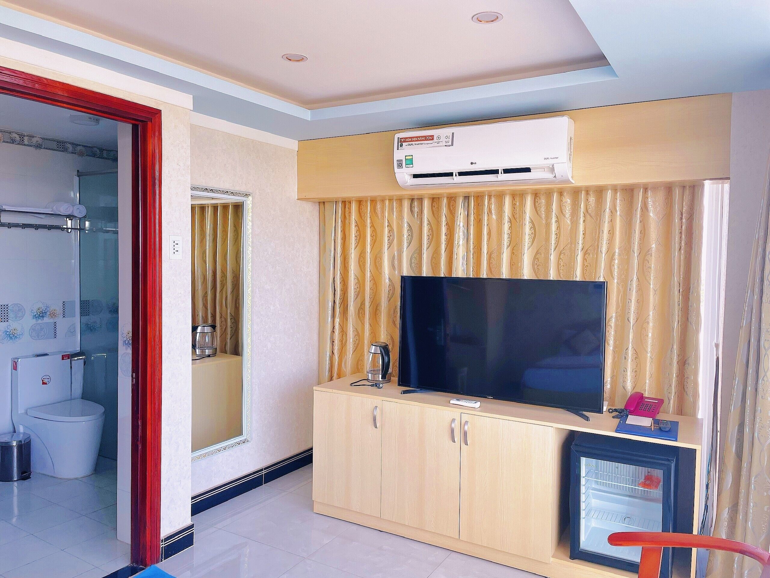 A hotel room with a TV, minibar, and a bathroom visible through an open door.
