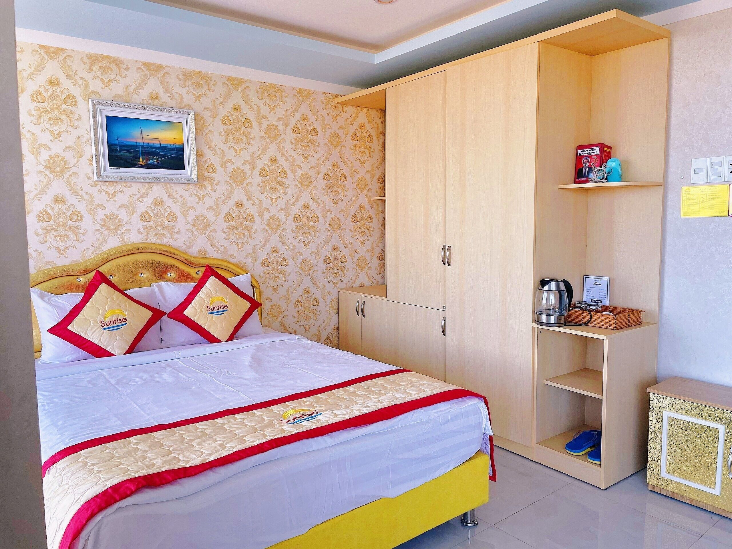 A neatly made bed with a headboard, a wardrobe, a shelf with items, and a framed picture on the wall.