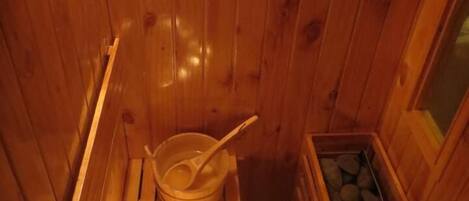 A wooden sauna with a wooden bench, a bowl with a ladle, and a container of stones.