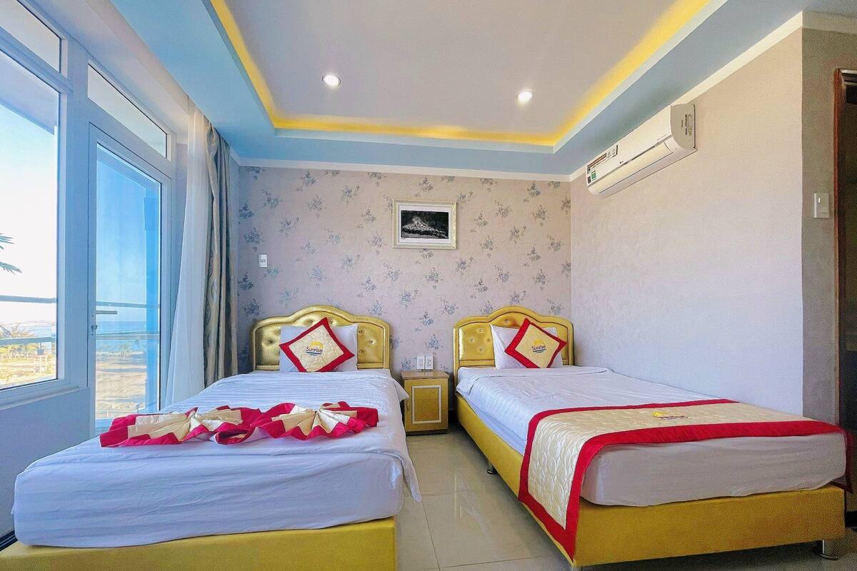A hotel room with two beds, a large window, and a ceiling light fixture.