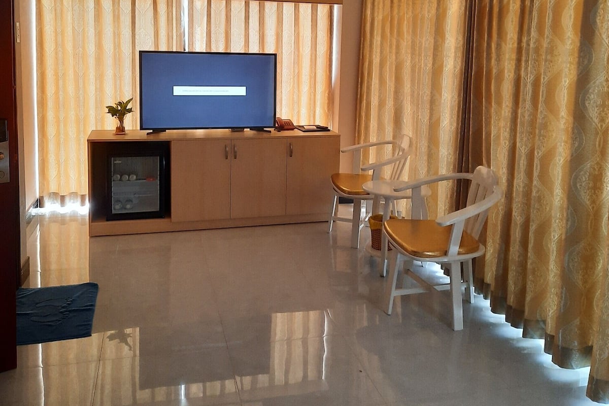 A modern living room with a flat-screen TV, a built-in air conditioner, and a seating area with two white chairs.