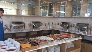 Montaje de bufé con distintas estaciones de comida, que incluyen opciones calientes y frías, y una máquina de café de servicio propio.