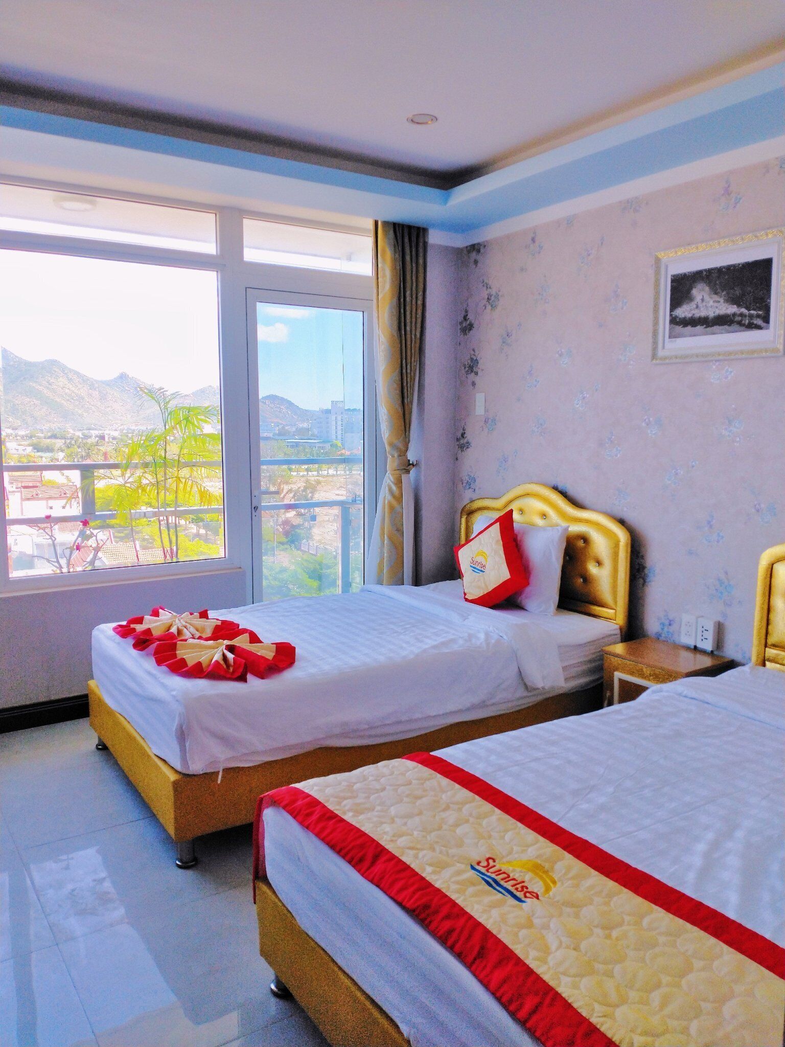 A hotel room with two beds, a large window with a view of mountains, and a framed picture on the wall.