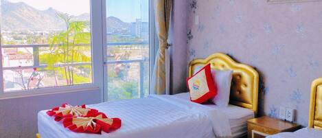 A hotel room with two beds, a large window with a view of mountains, and a framed picture on the wall.