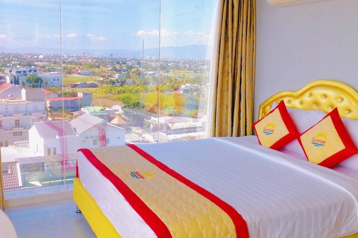 A hotel room with a large bed, a view of a cityscape, and an air conditioning unit on the wall.