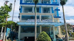 Un hotel de varios pisos con fachada azul y blanca, llamado SUNRISE HOTEL.