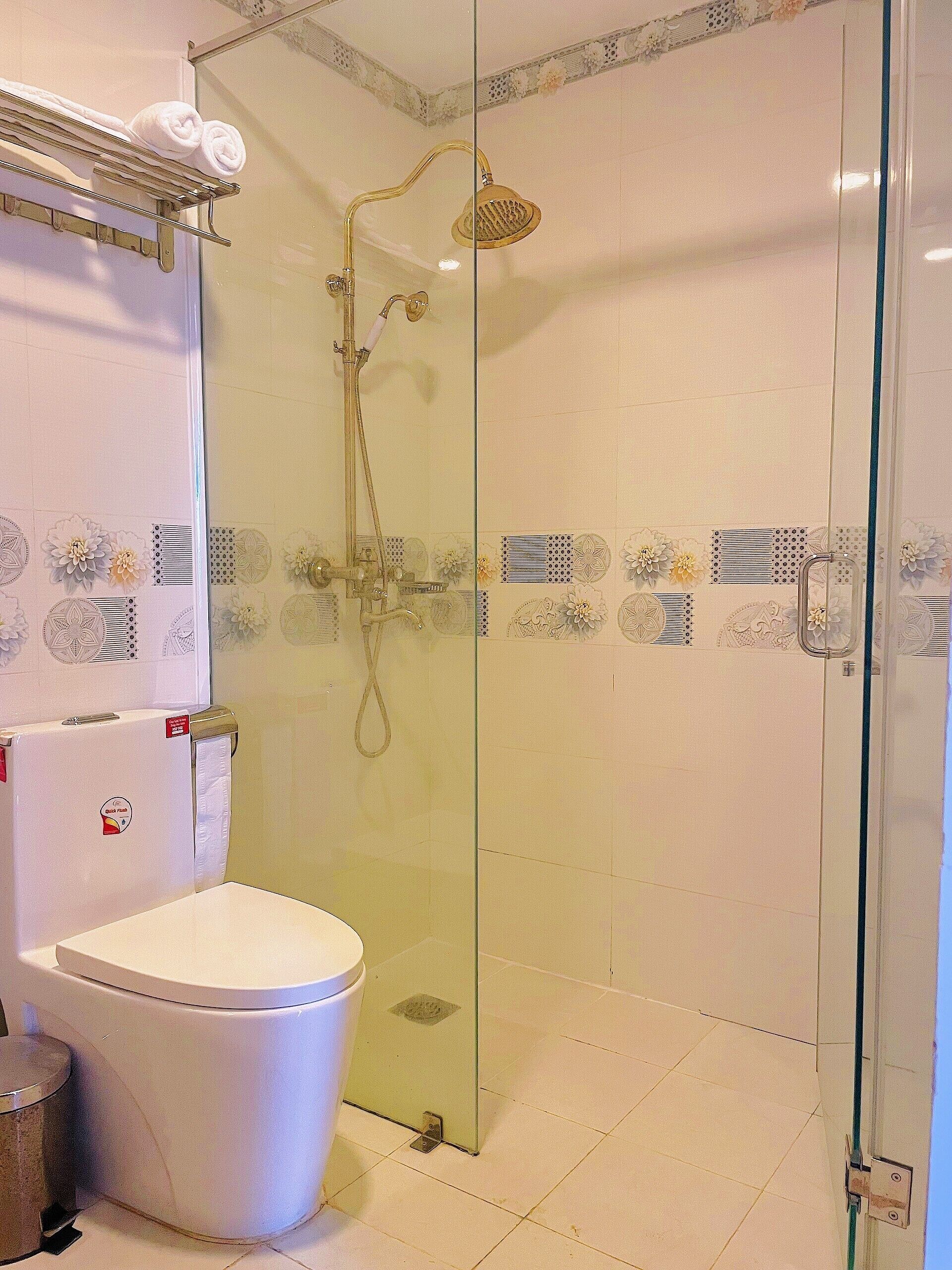 Ein Badezimmer mit einer Glaskabine zur Dusche, einer Toilette und einem Handtuchhalter mit Handtüchern.