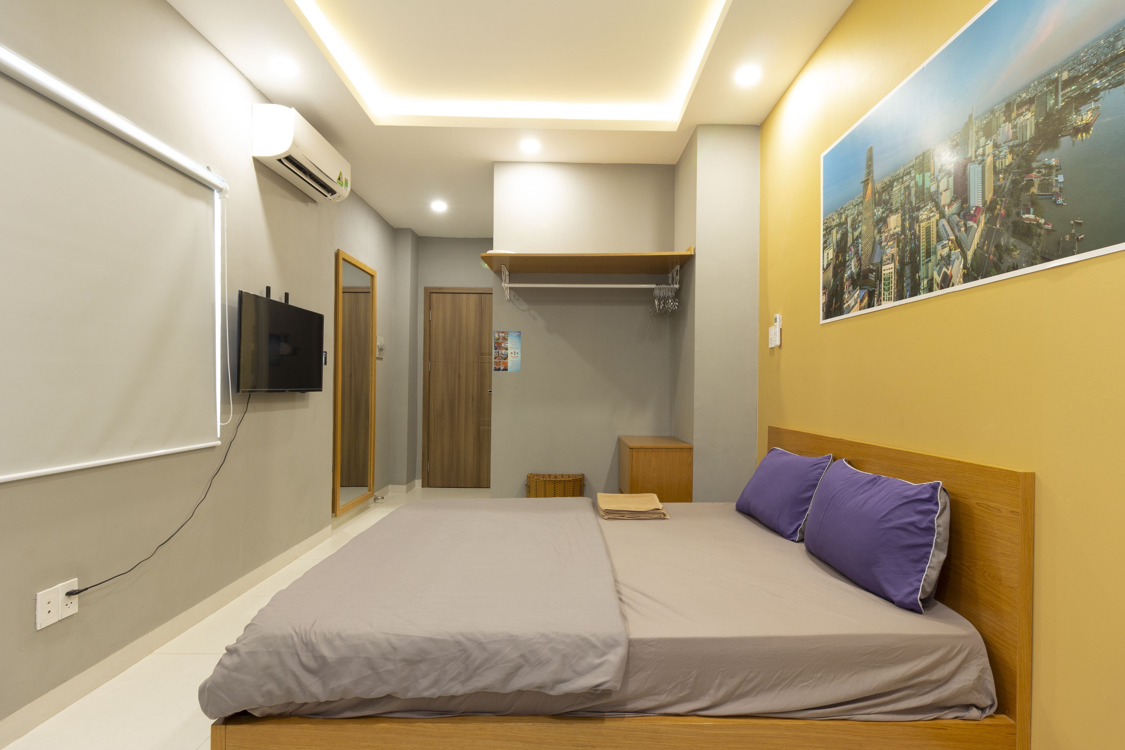 A modern bedroom with a large bed, a mounted TV, and a cityscape painting on the wall.