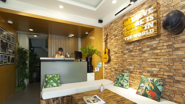 Un vestíbulo con mostrador de recepción, área de madera para la recepción, zona de estar con cojines, una mesa de centro y una guitarra en la pared.