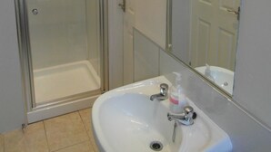 A bathroom with a glass-enclosed shower, a white sink, and a mirror. - Jasmine Central Guest House (Aberdeen)