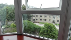 A room with a large window overlooking a residential area, featuring a stone wall and greenery. - Jasmine Central Guest House (Aberdeen)