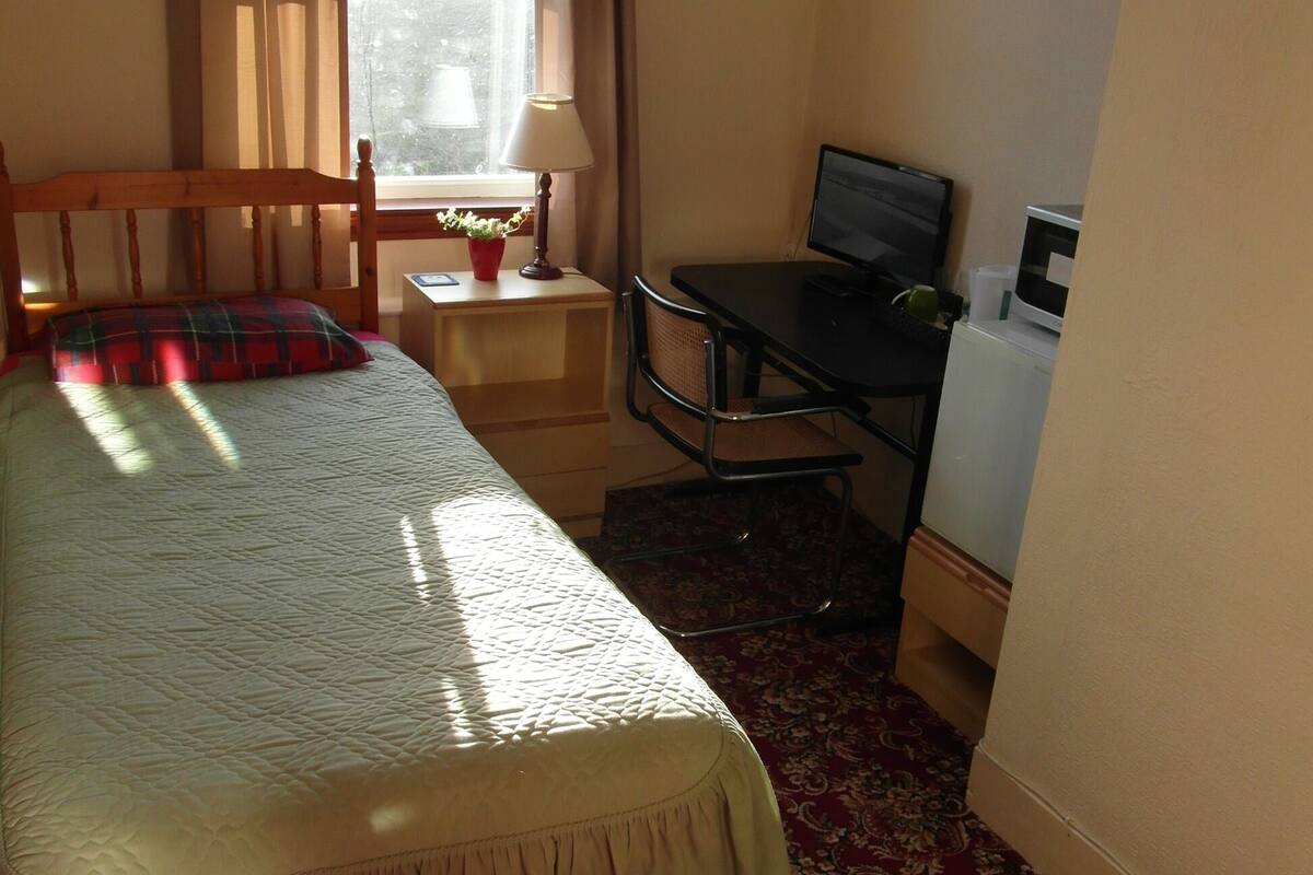 Habitación de hotel con cama, escritorio con computadora, lámpara y ventana con cortinas.