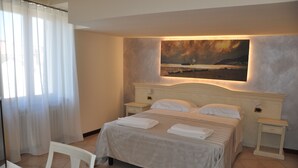 Una cama bien hecha con sábanas blancas, una mesita de noche con lámpara y un cuadro de un paisaje en la pared.