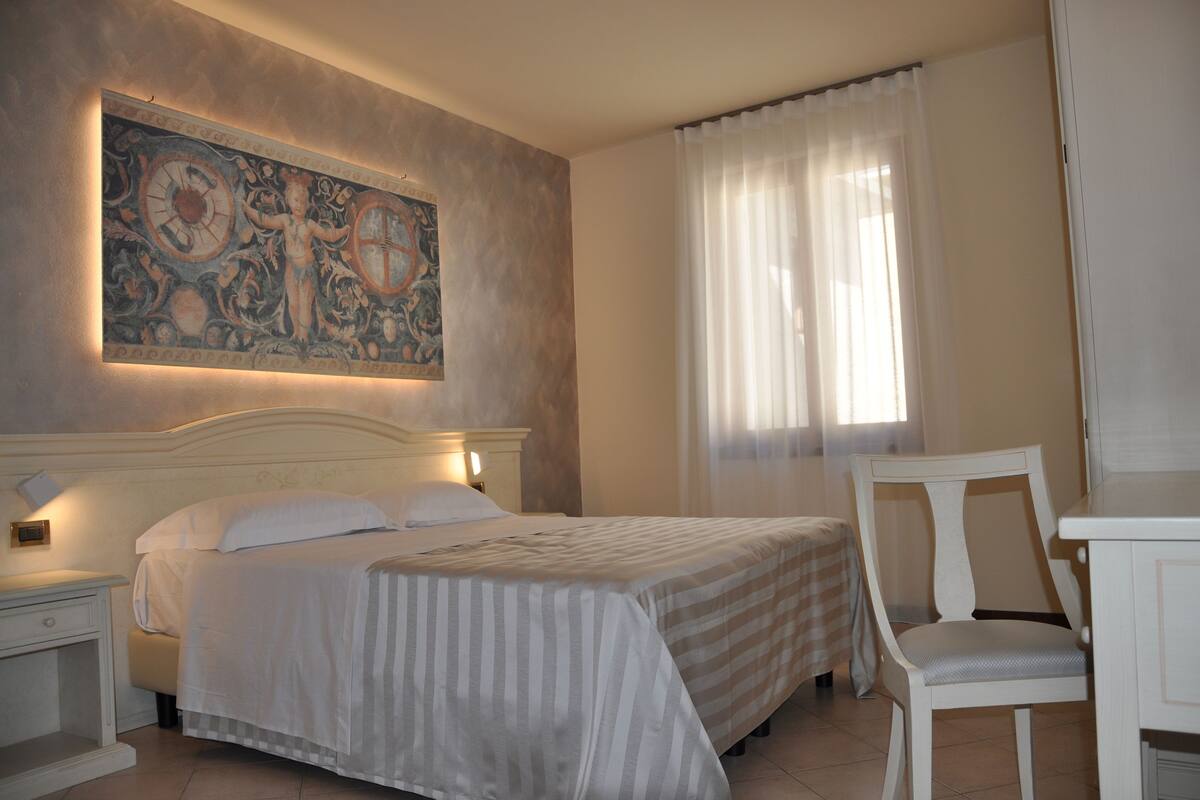 A hotel room with a large bed, a chair, a desk, and a painting on the wall.