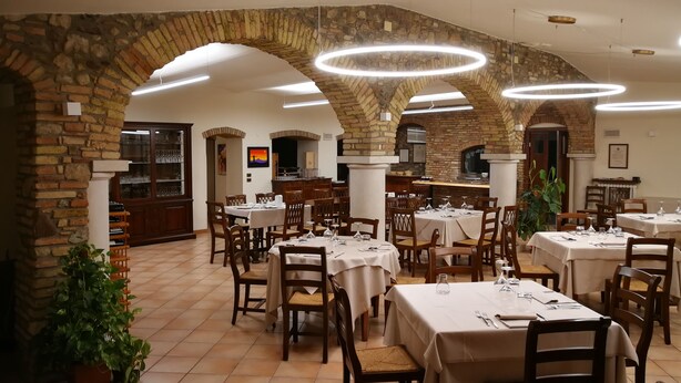Un restaurante con arcos de ladrillo, mesas redondas y sillas, suelo de baldosas y vistas a la cocina.