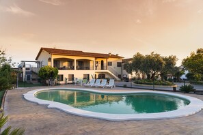 En stor bolig med swimmingpool, udendørs møbler og en overdækket terrasse.