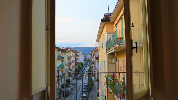 A view from a window overlooking a narrow street lined with multi-story buildings, featuring balconies and parked cars. - Dimora Paternò (Caserta)