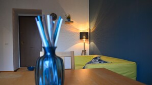 A room with a wooden table, a blue vase, a lamp, a bed with a yellow blanket, and a wall clock. - Dimora Paternò (Caserta)