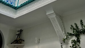 Un interior de varios niveles con ornamentales detalles en blanco y azul, un balcón con barandilla intrincada y una planta colgante.