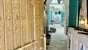 Un interior lujoso con una puerta dorada que indica “Riad Mille et une Couleurs”, que da a un espacio amplio con paredes color turquesa y un suelo con diseño.