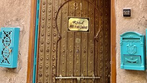 Fachada rústica de un edificio con una gran puerta de madera marcada con el número 91, un cartel que dice 
